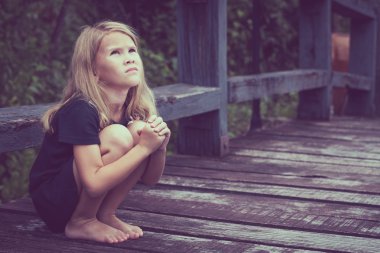 Portrait of sad blond little girl sitting on the bridge