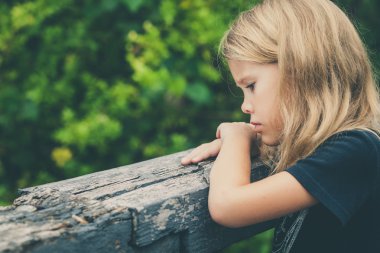 Portrait of sad blond little girl sitting on the bridge