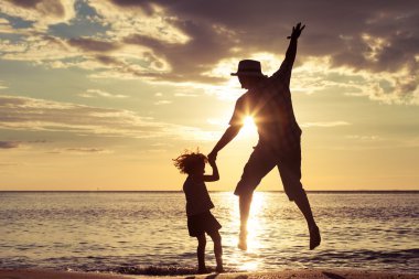 Father and son playing on the beach at the sunset time. clipart