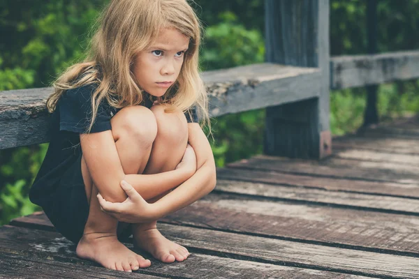 Ritratto di bambina bionda triste seduta sul ponte — Foto Stock