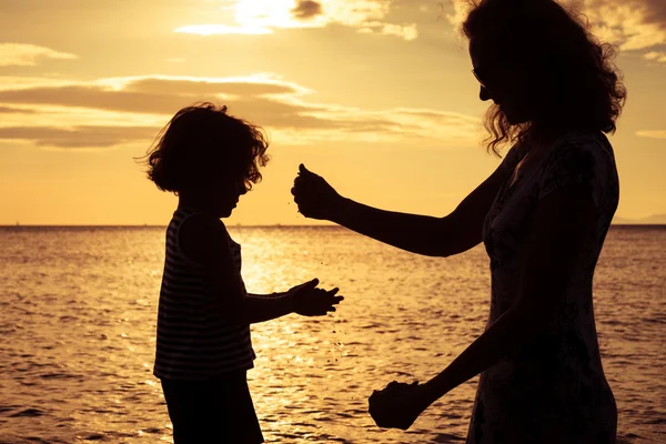 Mor och son spelar på stranden vid solnedgången tid. — Stockfoto