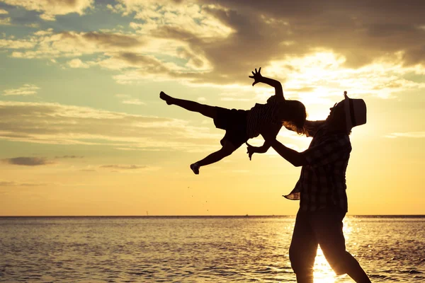 Vader en zoon spelen op het strand op de zonsondergang keer. — Stockfoto