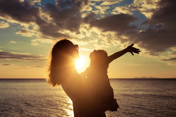 Mãe e filho brincando na praia na hora do pôr do sol . — Fotografia de Stock