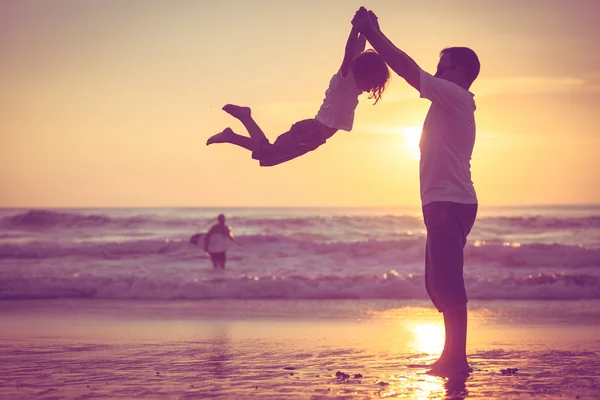 Far och son som spelar på stranden vid solnedgången tid. — Stockfoto