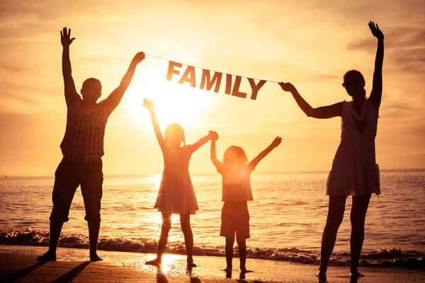 Glad familj stående på stranden vid solnedgången tid. — Stockfoto