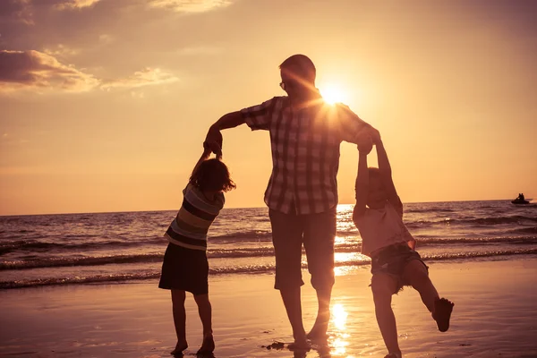 Otce a děti si hrají na pláži při západu slunce. — Stock fotografie