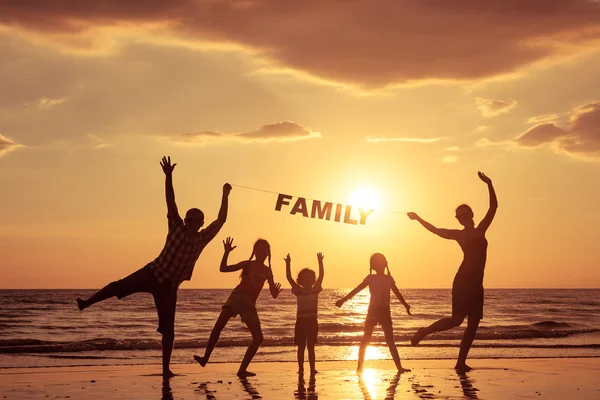 Glad familj stående på stranden vid solnedgången tid. — Stockfoto