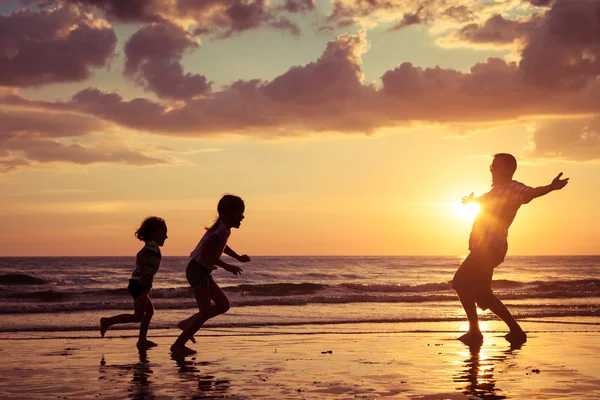 Vader en kinderen spelen op het strand op de zonsondergang keer. — Stockfoto