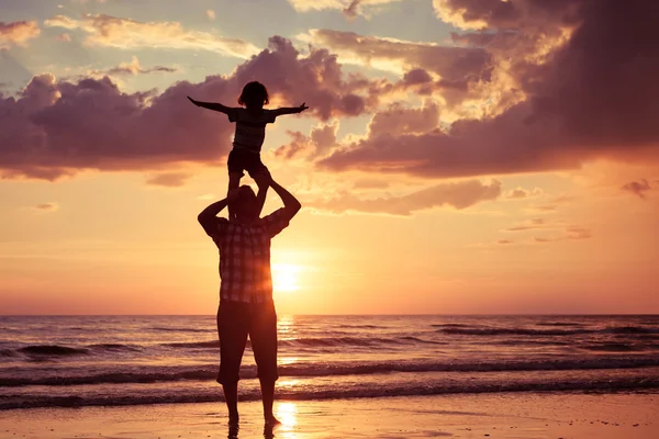 Otec a syn hraje na pláži při západu slunce. — Stock fotografie