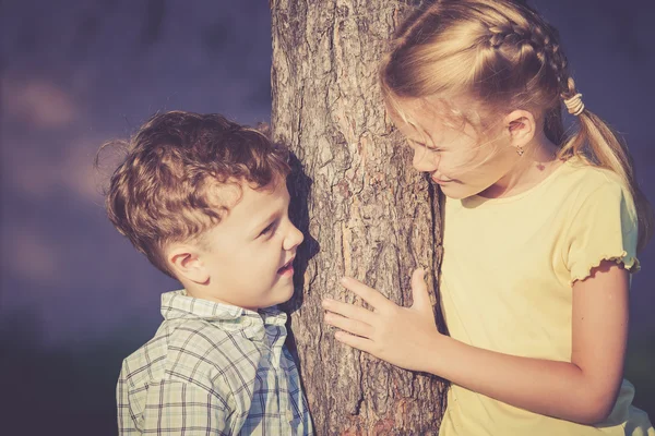 Duas crianças felizes brincando perto da árvore no dia . — Fotografia de Stock