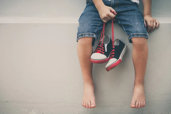 Mały chłopiec siedzi w pobliżu domu i utrzymanie sneaker młodzieży — Zdjęcie stockowe