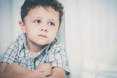 Pencerenin oturan üzgün küçük çocuk portresi