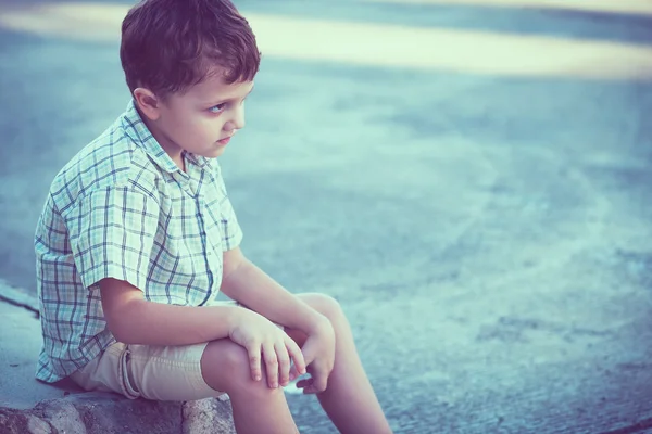 Portrait of sad little boy sitting on street — Stock Photo, Image