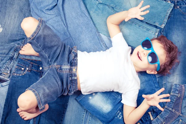 Söt liten pojke med solglasögon på bakgrunden jeans. — Stockfoto