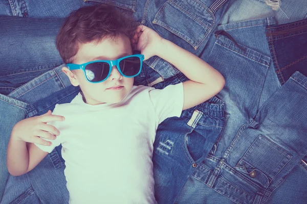Ragazzino carino con occhiali da sole sullo sfondo jeans . — Foto Stock