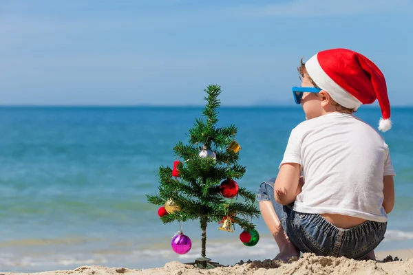 Gelukkig jongetje zittend op het strand op het moment van de dag. — Stockfoto