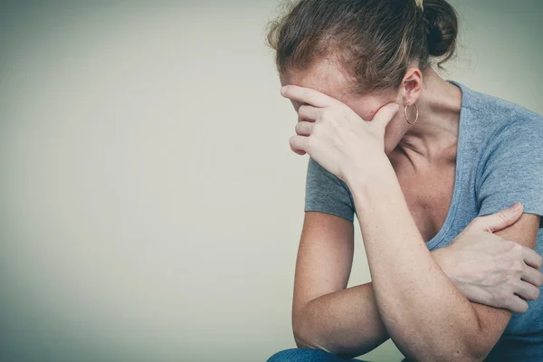 Una mujer triste sentada cerca de una pared — Foto de Stock