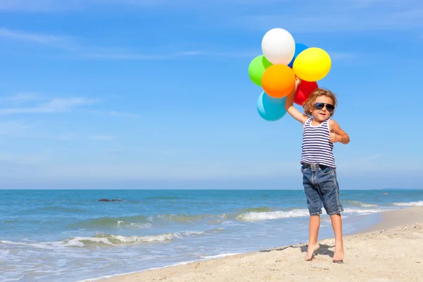 Liten pojke med ballonger stående på stranden — Stockfoto