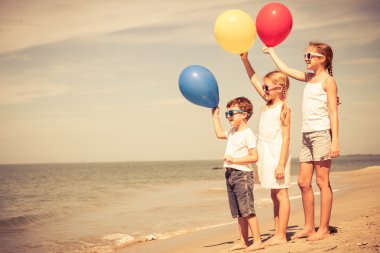 Plajda durup balonlarla üç mutlu çocuk
