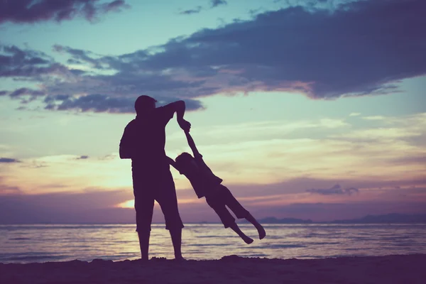 Far och son som spelar på stranden vid solnedgången tid. — Stockfoto