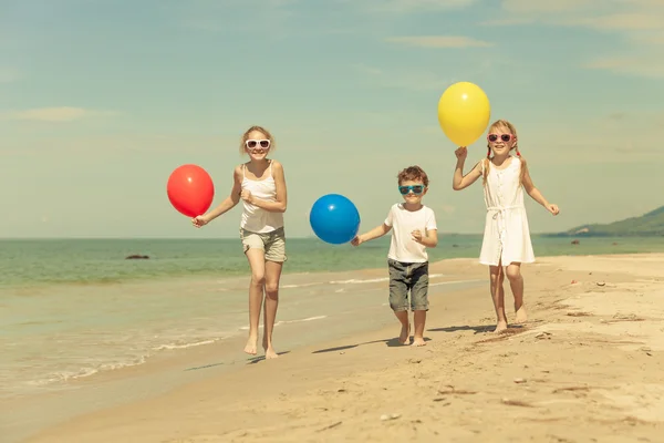 Três crianças felizes com balões correndo na praia no d — Fotografia de Stock