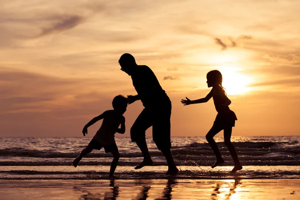 Otce a děti si hrají na pláži při západu slunce. — Stock fotografie