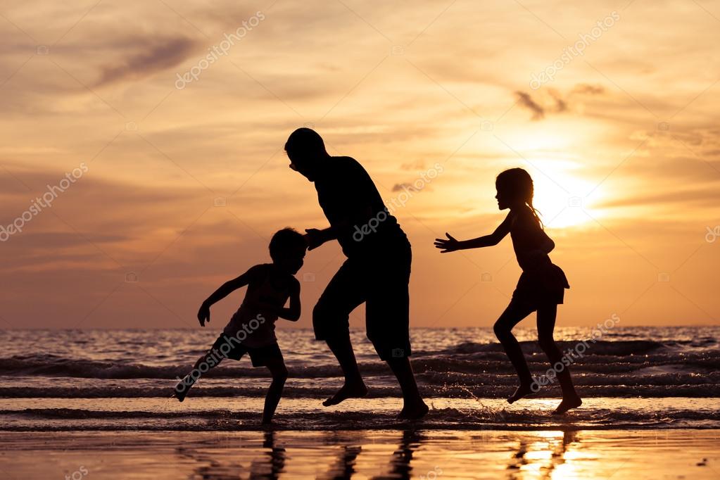 Father and children playing on the beach at the sunset time
