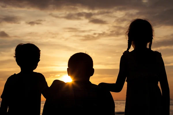 Pai e crianças brincando na praia na hora do pôr do sol . — Fotografia de Stock