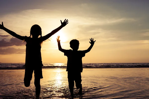 Crianças felizes brincando na praia na hora do pôr do sol . — Fotografia de Stock