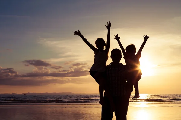 Pai e crianças brincando na praia na hora do pôr do sol . — Fotografia de Stock