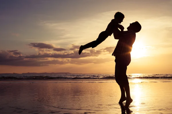 Vader en zoon spelen op het strand op de zonsondergang keer. — Stockfoto