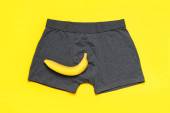 Kreativní koncept mužské potence. Šedé bavlněné kalhotky, čerstvý banán na žlutém pozadí ploché ležel horní pohled. Zdraví mužů, zdravý sexuální život, dobrá síla. Urologie, sexuolog, psychoterapeutická léčba.