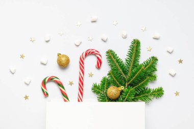 Noel şekeri bastonu, yeşil köknar dalları, altın toplar, hediye çantası, konfeti yıldızları, beyaz arka planda şekerleme düz bir görünümde yatıyordu. Yeni yıl konsepti. Şölen dekoru, tatil kartı. Kutlama 2021.