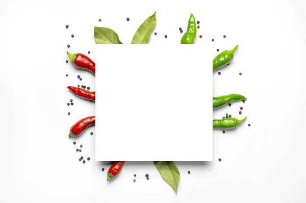 Creative food layout. Hot red and green fresh chili peppers Bay leaf dry black peppercorns, white blank sheet of paper on white background flat lay top view. Spicy spices for cooking, cayenne pepper.