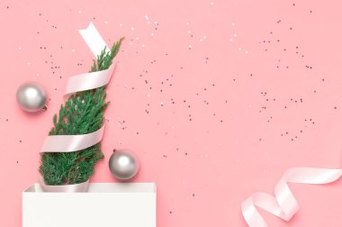 Yeni yıl kompozisyonu, kış dekorasyonu. Gümüş Noel oyuncak topları, tatil kurdeleleri, Noel ağacı dalları pembe arka planda beyaz hediye çantası. Düz görünüm kopyalama alanı yatıyordu. Kutlama konsepti.