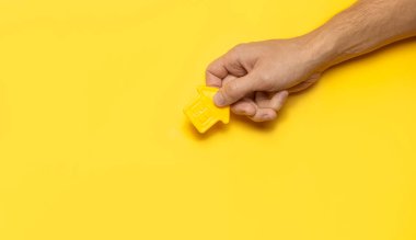 Sarı arka plandaki ev sembolü üst tarafta yatıyordu. Plastik sarı bir ev modeli. Ev ve daire alma kavramı. Ev kiralamak, gayrimenkul. İpotek, emlak sigortası..