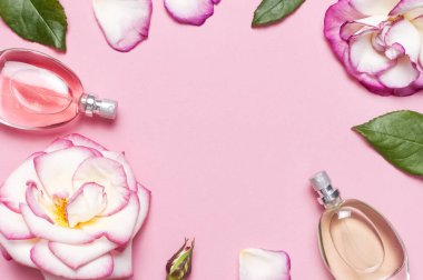 Parfüm ve çiçeklerle güzel bir kompozisyon. Parfüm şişeleri, gül çiçekleri... Pembe arka planda yeşil yapraklar... Kozmetik parfümü tuvalet suyu parfümü koleksiyonu.