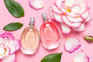 Parfüm ve çiçeklerle güzel bir kompozisyon. Parfüm şişeleri, gül çiçekleri... Pembe arka planda yeşil yapraklar... Kozmetik parfümü tuvalet suyu parfümü koleksiyonu.