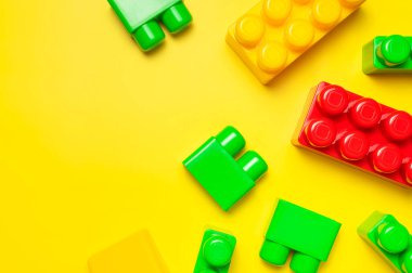 Sarı arka planda çok renkli plastik çocuk inşaatçısı. İnşaat için renkli çocuk tuğlaları. Düz görünüm kopyalama alanı yatıyordu. Plastik bina arka planı blokluyor. Oyuncak geliştirme, oyun