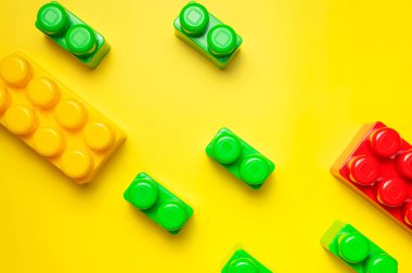 Sarı arka planda çok renkli plastik çocuk inşaatçısı. İnşaat için renkli çocuk tuğlaları. Düz görünüm kopyalama alanı yatıyordu. Plastik bina arka planı blokluyor. Oyuncak geliştirme, oyun