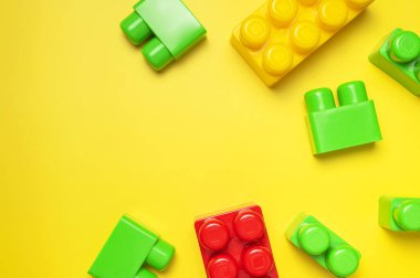 Sarı arka planda çok renkli plastik çocuk inşaatçısı. İnşaat için renkli çocuk tuğlaları. Düz görünüm kopyalama alanı yatıyordu. Plastik bina arka planı blokluyor. Oyuncak geliştirme, oyun