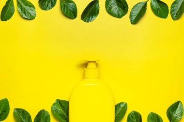 Doğal organik kozmetik. Güzellik, kaplıca, markalaşma modelleri. Sarı kozmetik şişe kabı. Sarı arka planda taze yeşil yapraklar. Minimalist ambalaj eko kozmetik konsepti