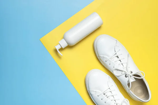 White leather sneakers, plastic bottles of cleaning products for shoes on blue yellow background flat lay top view. Natural leather shoe care, spray, foam, shoe deodorant, cosmetic shoe products.