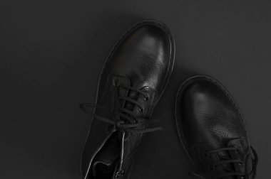 Siyah arka planda şık siyah deri çizmeler düz manzarada yatıyordu. Tarz sahibi kadınların erkek üniformaları. Ayakkabı bağcıklı Grunge çizmeleri. Kıyafetler, ayakkabılar, moda geçmişi. Klasik deri ayakkabılar..