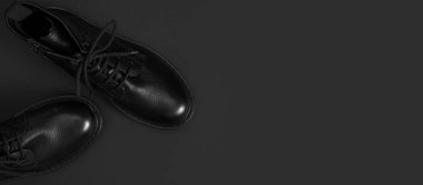 Siyah arka planda şık siyah deri çizmeler düz manzarada yatıyordu. Tarz sahibi kadınların erkek üniformaları. Ayakkabı bağcıklı Grunge çizmeleri. Kıyafetler, ayakkabılar, moda geçmişi. Klasik deri ayakkabılar..