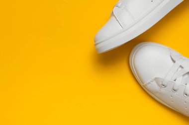 Sarı arka planda beyaz kadın deri spor ayakkabıları düz yerde yatıyordu. Şık gençlik ayakkabıları, spor ayakkabıları, hakiki deri ayakkabılar. Minimalist ayakkabı mağazası reklamcılığı moda ayakkabısı arka planı.