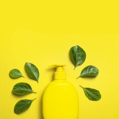 Doğal organik kozmetik. Güzellik, kaplıca, markalaşma modelleri. Sarı kozmetik şişe kabı. Sarı arka planda taze yeşil yapraklar. Minimalist ambalaj eko kozmetik konsepti.