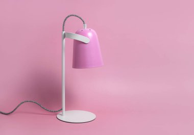 Pembe arka plandaki modern masa lambası düzdü. Işık, lamba, ışık, iç dekorasyon, elektrik. Çocukların pembe masa lambası. Tek parça mobilya. Metal tasarımcı lamba.