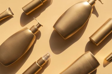 Bej arka planda güneş gölgeleri olan altın gibi temiz kozmetik şişeleri. Kozmetik şişeleri, tüpleri taklit ediyor. Marka ürünleri, spa, güzellik geçmişi. Düz görünüm kopyalama alanı yatıyordu. Tasarladığınız yer.