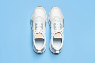 Mavi arka planda bir çift açık renk erkek ayakkabısı. Spor ayakkabıları, spor ayakkabıları, spor ayakkabıları, koşu, antrenman. Spor ayakkabılarla minimalist bir geçmişi var. Sağlıklı yaşam tarzı kavramı. Düz görünüm kopyalama alanı.
